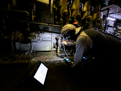 PSNERGY field technician tuning industrial furnace with headlamp and laptop